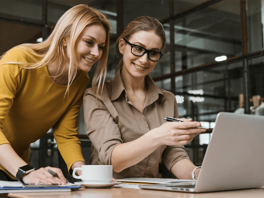 Duas profissionais sorrindo enquanto colaboram em um notebook.