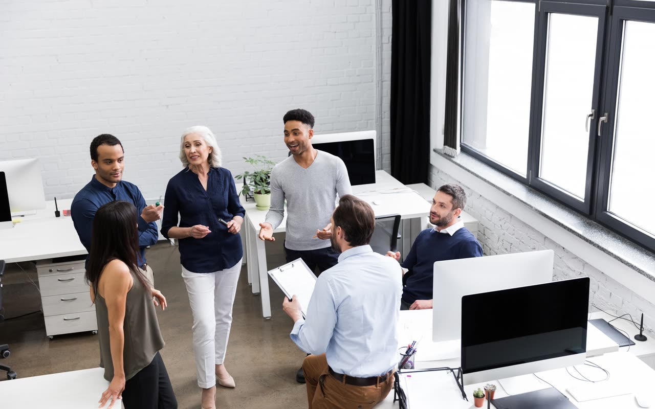 Equipe diversa reunida em um escritório, conversando de pé.